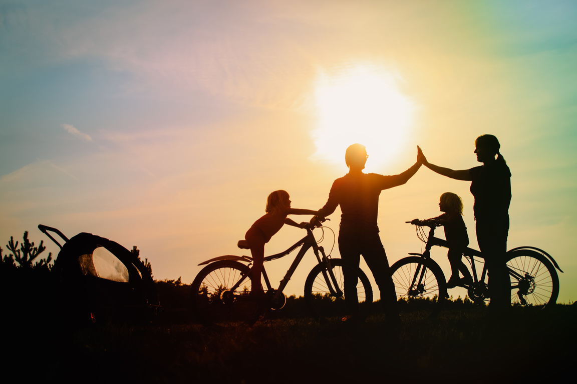 happy family -mother, father and two kids riding bike at sunset